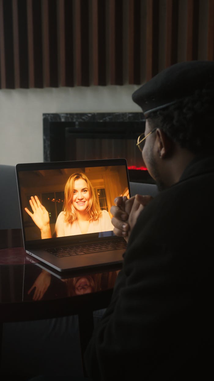 A virtual video call with a woman smiling and waving, showcased on a laptop screen.